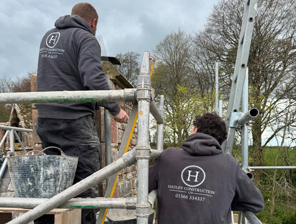 two construction workers on scaffolding measuring a wall with tools in their hands during a building project showcasing teamwork and construction skills 3 steps to success
